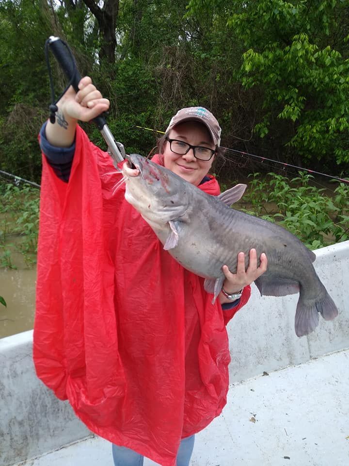 A woman in a red poncho is holding a large fish in her hands.