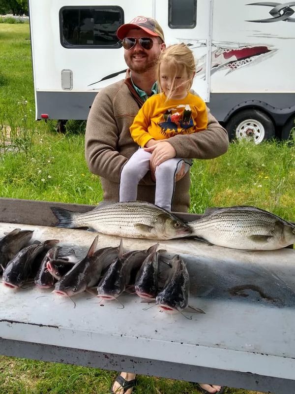 A man and a little girl are sitting on a table with fish.