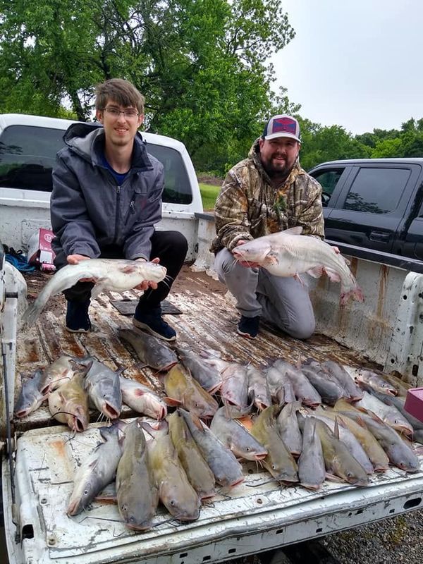 Two men are sitting in the back of a truck holding fish.