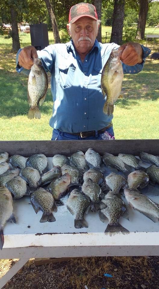 A man is holding two fish in front of a table full of fish.