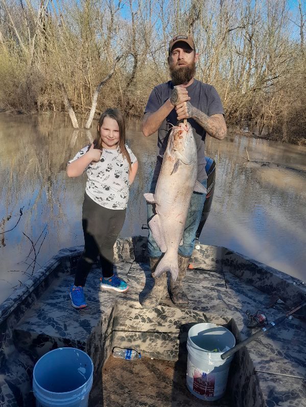 A man and a little girl are standing on a boat holding a large fish.