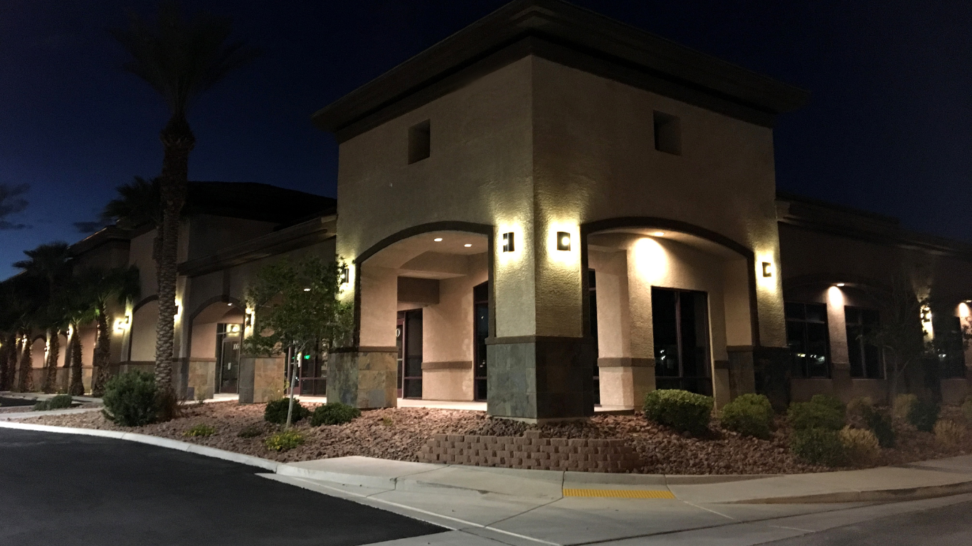Nighttime exterior view of a tan building with illuminated entryways, surrounded by palm trees and landscaping.