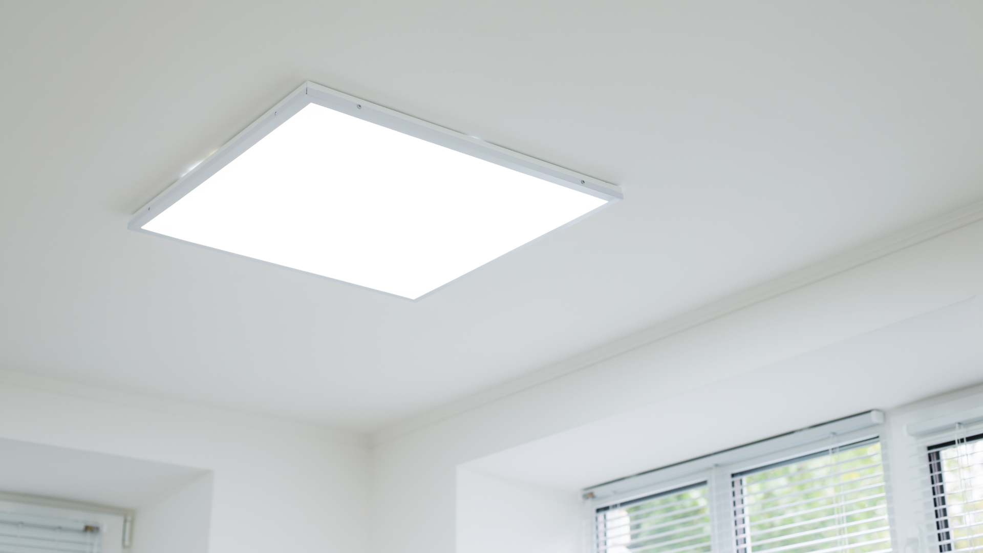 Bright, square LED ceiling light fixture in a white room; window on right.