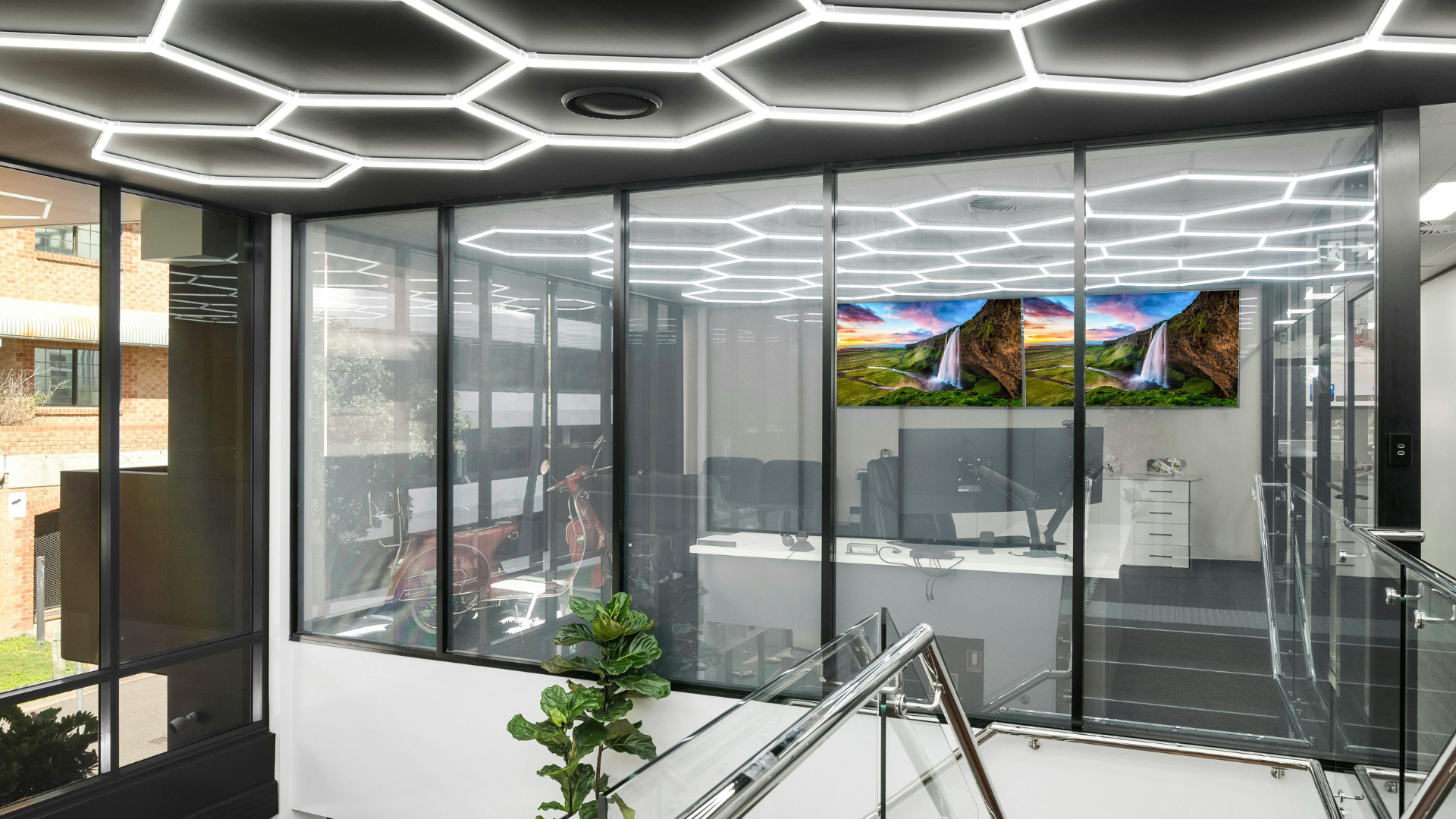 Modern office with glass walls, hexagon ceiling lights, and a waterfall display.