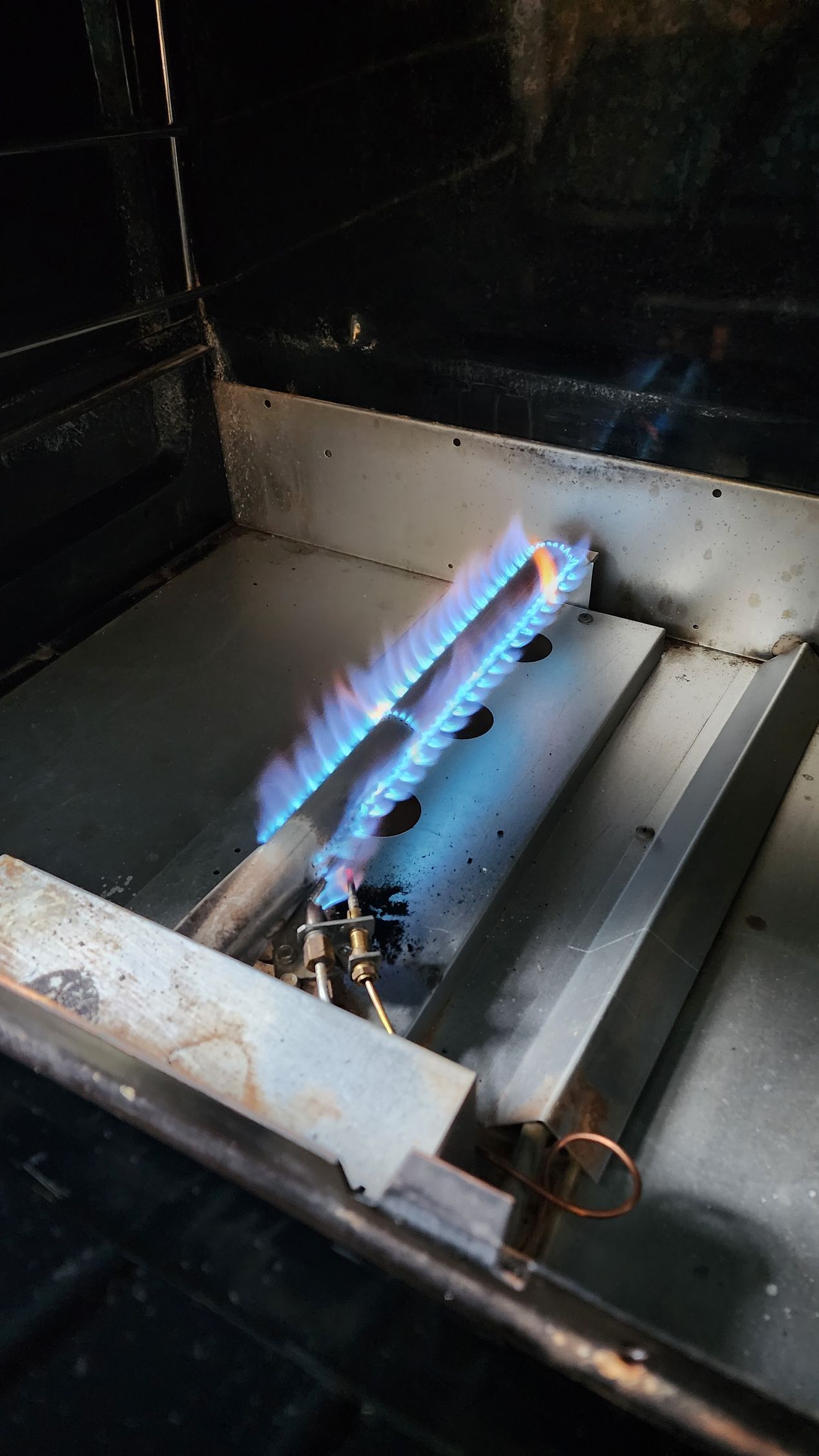 A bright blue gas flame burns from a metallic U-shaped burner inside a metal fire pit enclosure.