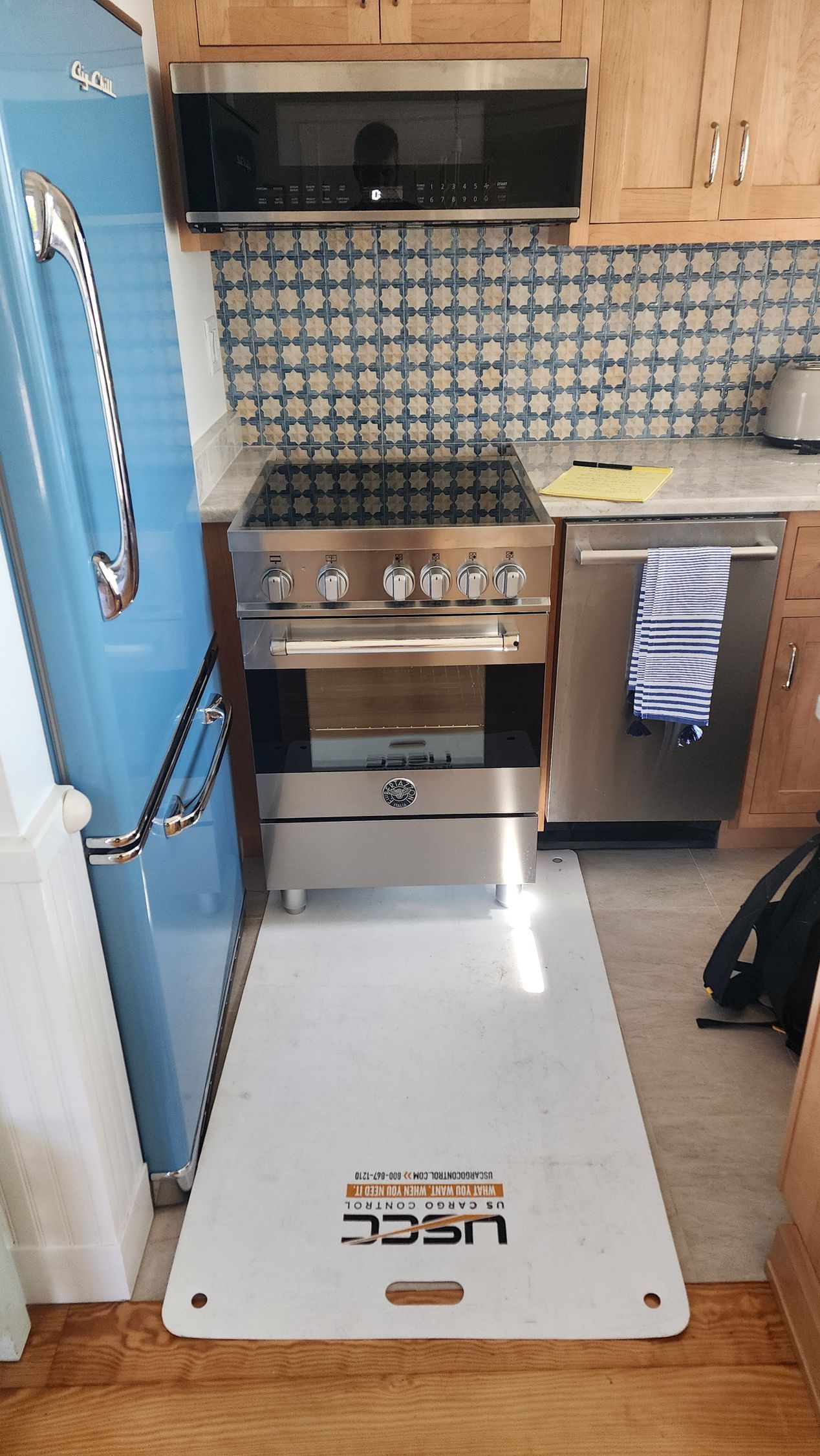 A stainless steel stove and dishwasher in a kitchen, with a protective white floor mat laid out in front of the stove.