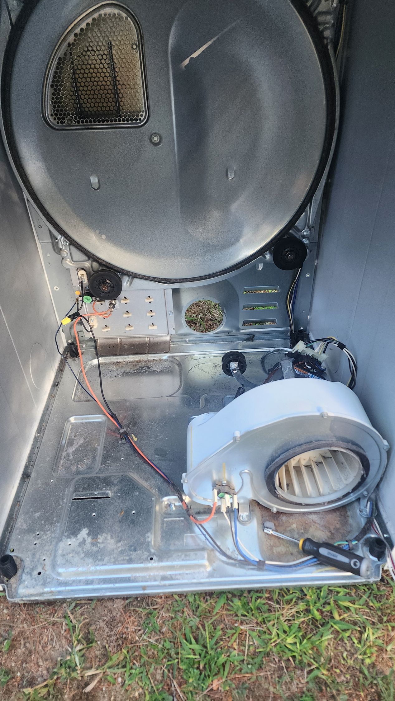 Interior view of a disassembled dryer with a blower housing and motor visible on a metal base, resting on grass.