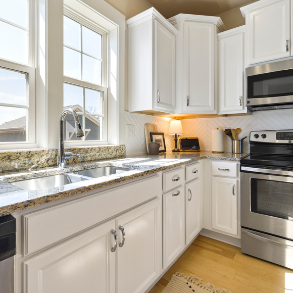 A modern kitchen features white cabinets, granite countertops, a stainless steel microwave and stove, and double windows.