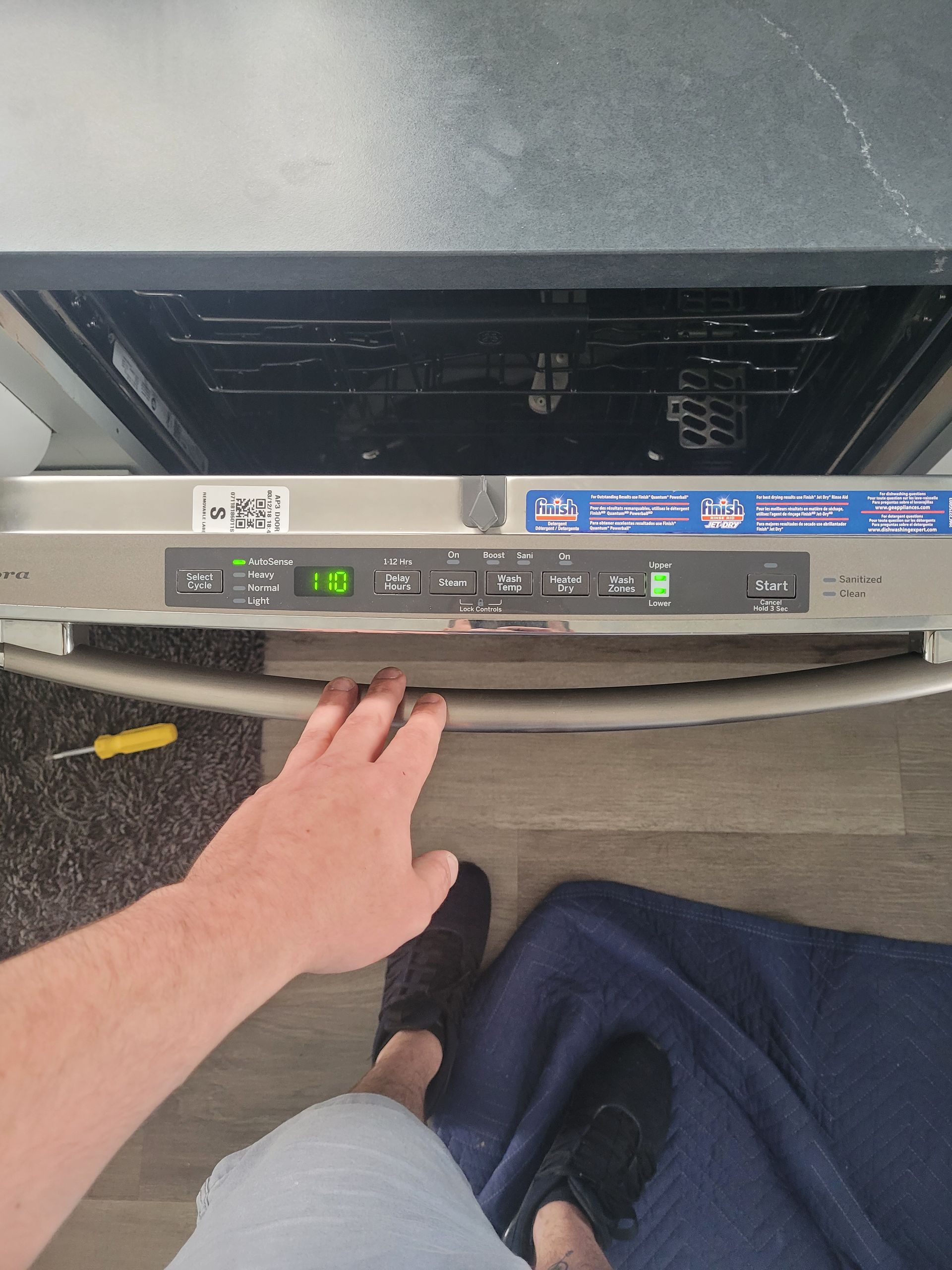 A person’s hand reaches toward the control panel of an open dishwasher in a kitchen.