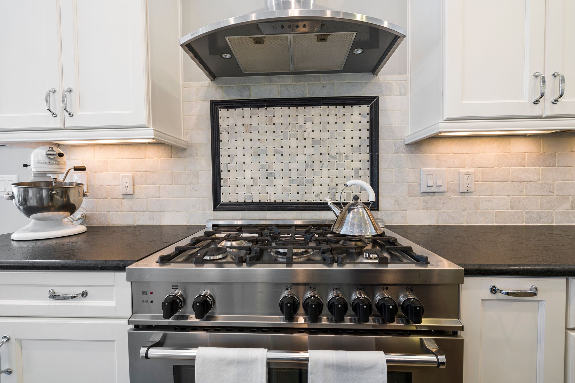 A modern kitchen features white cabinets, granite countertops, a stainless steel microwave and stove, and double windows.