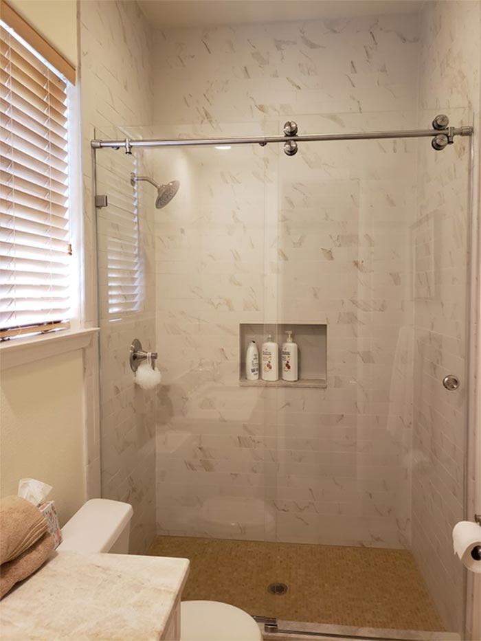 Modern bathroom with glass shower, white marble tile, toilet, and window.