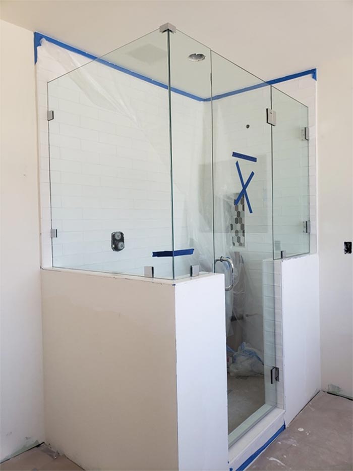 A corner shower with glass walls and a white base, still under construction. Blue tape is visible.