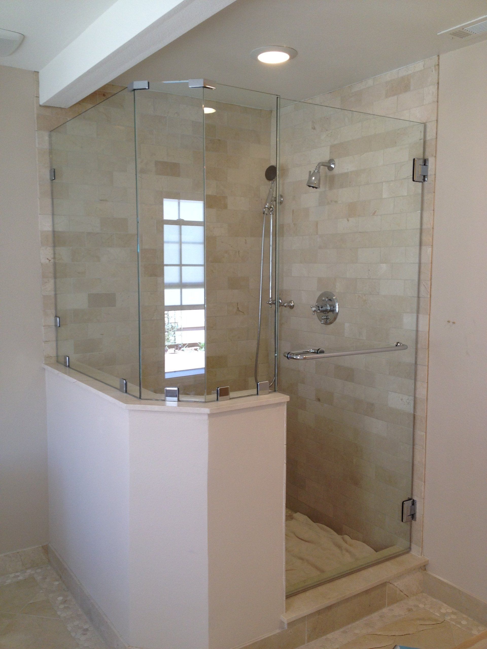 Glass-enclosed walk-in shower with beige tiled walls and a small window, situated in a bathroom.