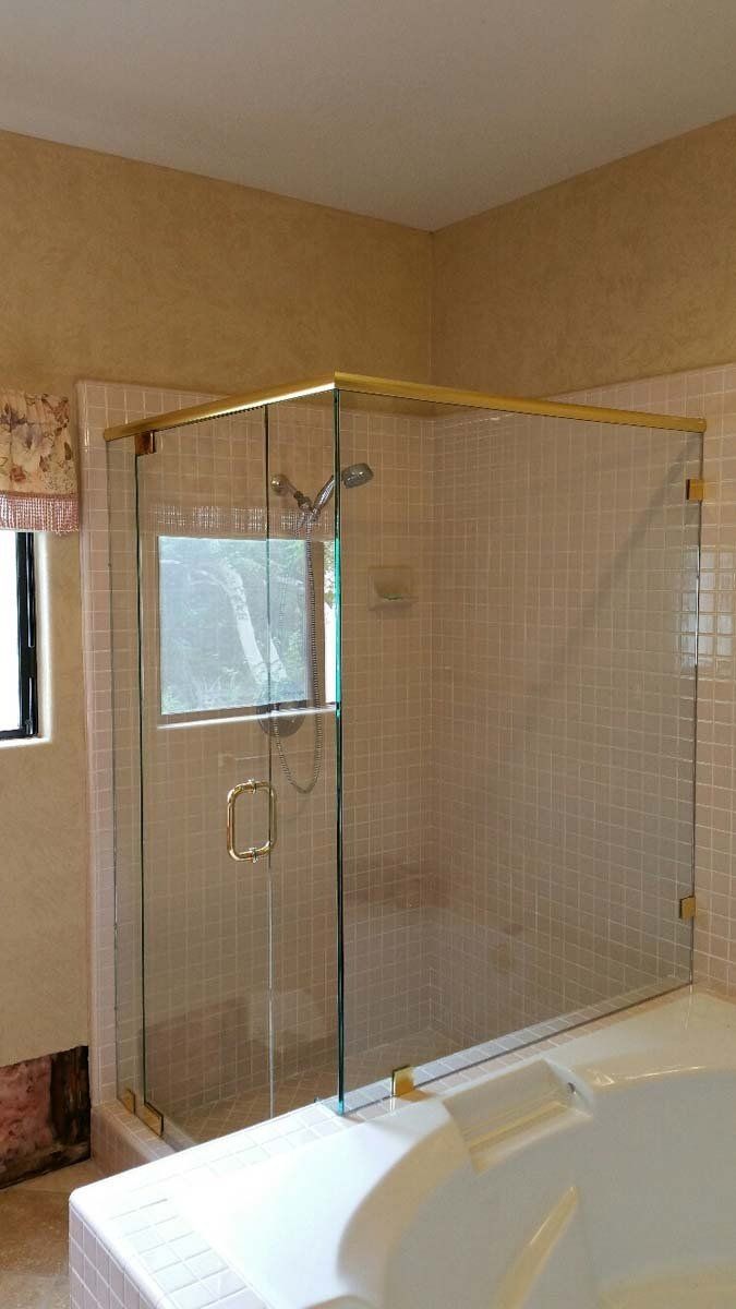Glass shower enclosure with gold framing in a bathroom, near a window and bathtub.