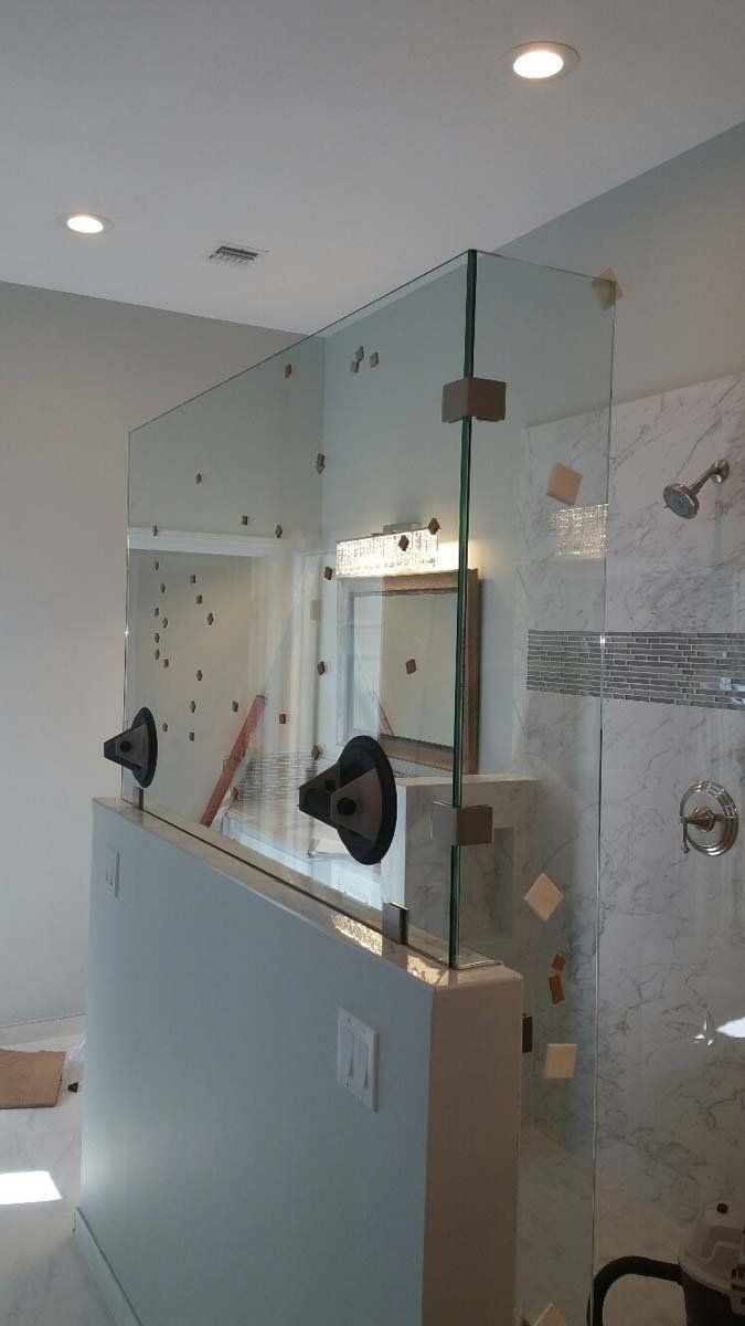 Glass shower enclosure with a half wall, light fixtures, and a vanity mirror.