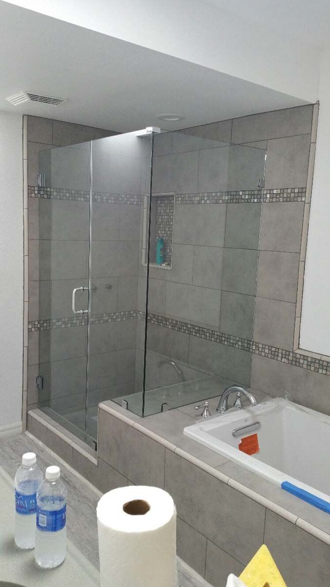 Bathroom with gray tiled walls, glass shower door, tub, and bottles of water.