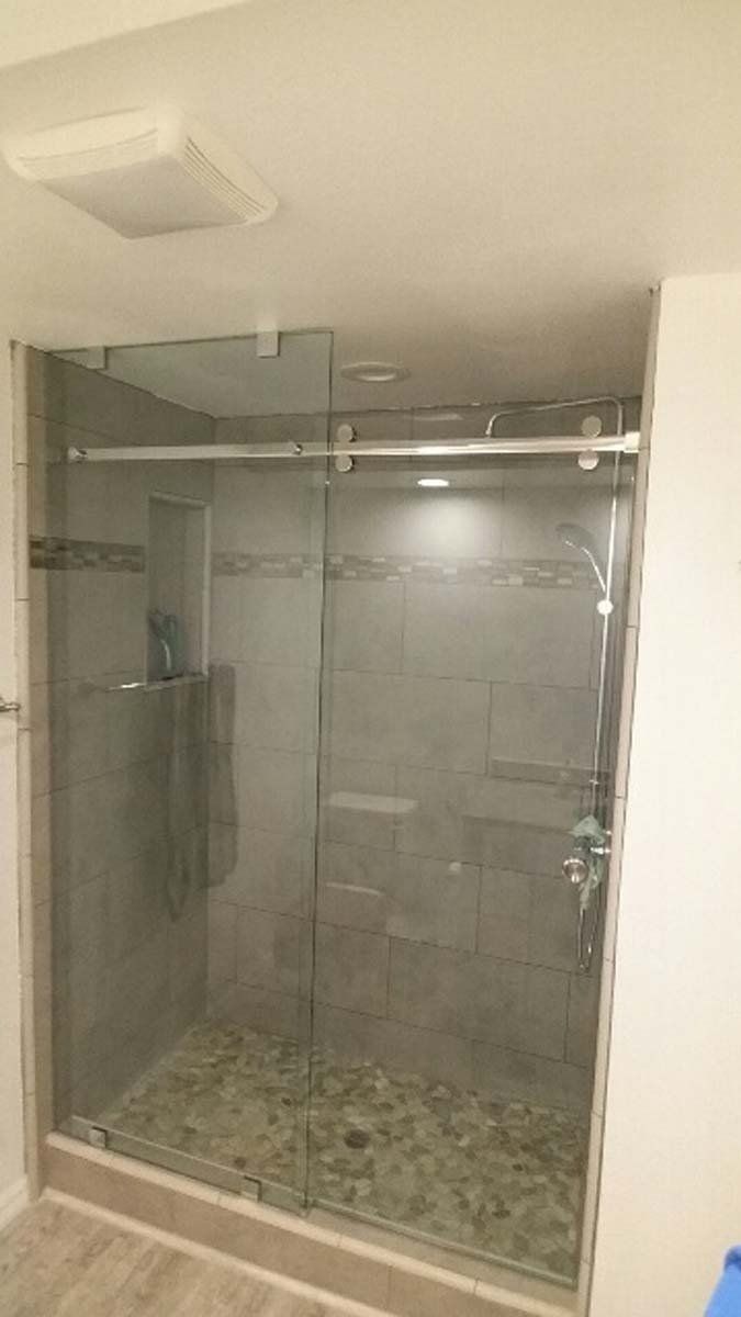 Glass shower enclosure with sliding doors, gray tile, and pebble floor.