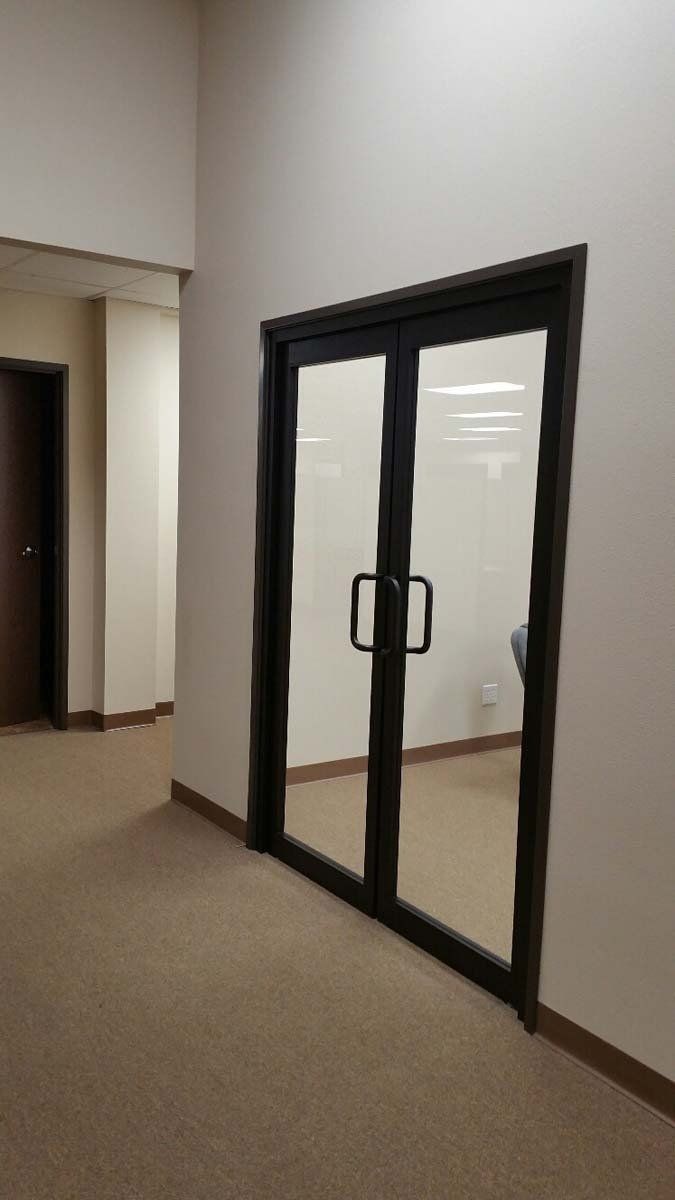 Glass double doors with black frames in a hallway with beige walls and carpet.
