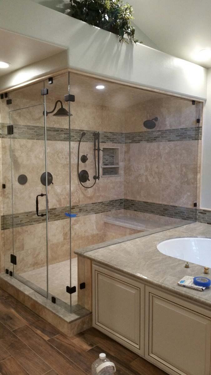 Shower with glass enclosure, tan tile, stone border, dark fixtures, adjacent to a vanity and bathtub.