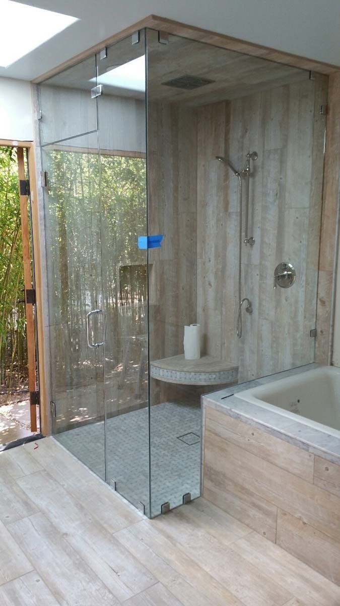 Glass shower with stone tile walls and a built-in bench, next to a bathtub.
