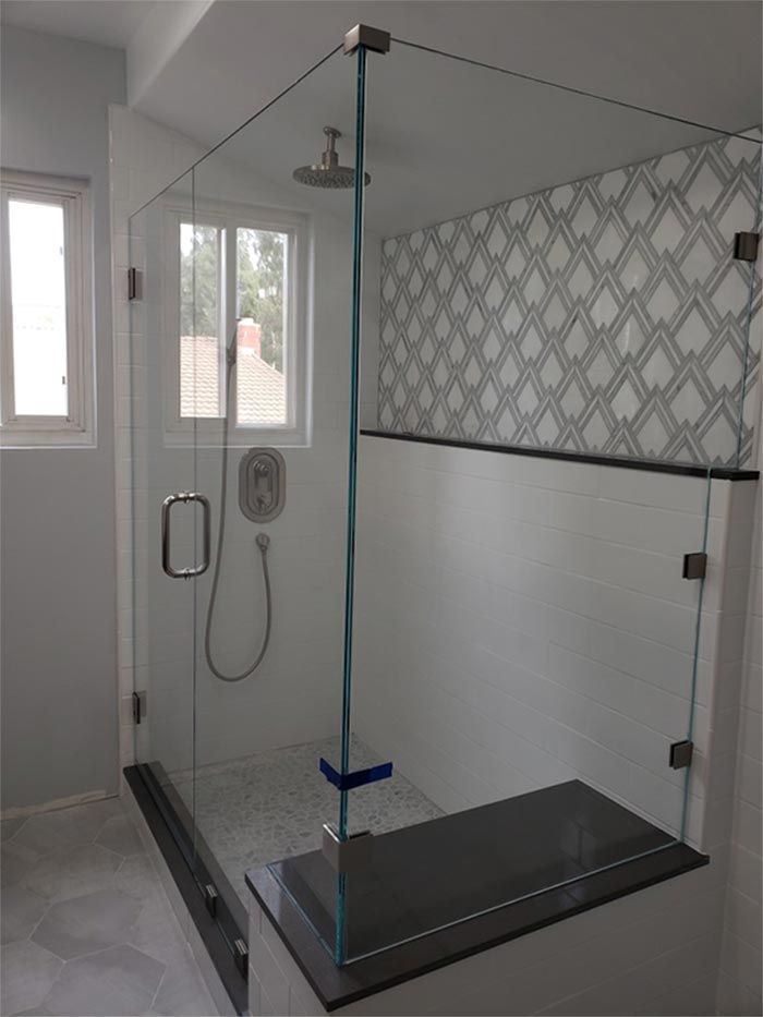 Glass shower with gray tile floor and patterned wall behind.