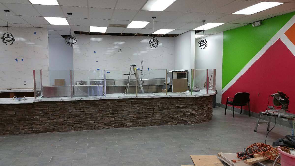 Restaurant interior under construction with a stone-faced counter, stainless steel equipment, and colorful accent wall.