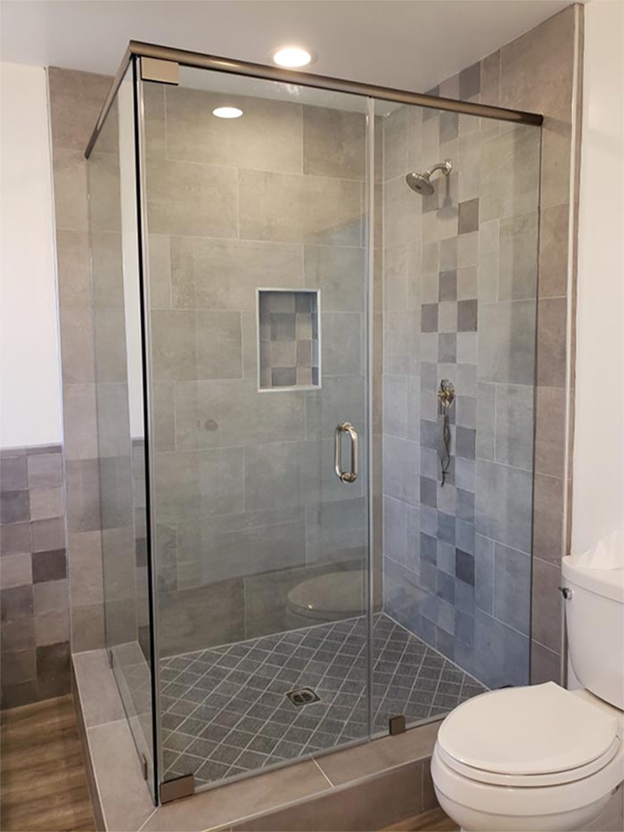 Glass shower with gray tiled walls and floor, white toilet in the corner.