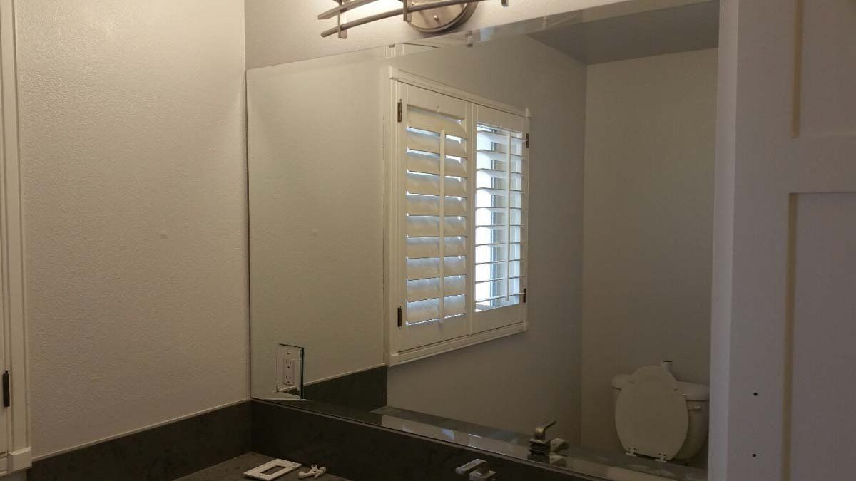 Bathroom with a large mirror, window with shutters, and a white toilet.