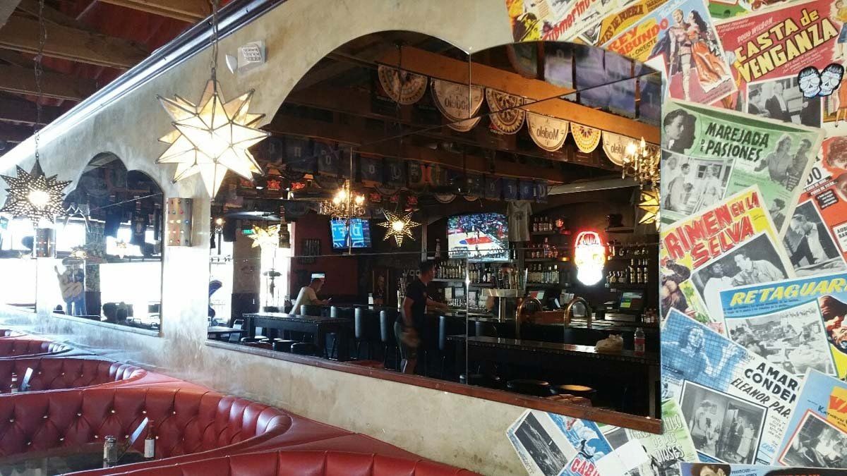 Mexican restaurant interior with red booths, bar, and colorful posters on the wall.