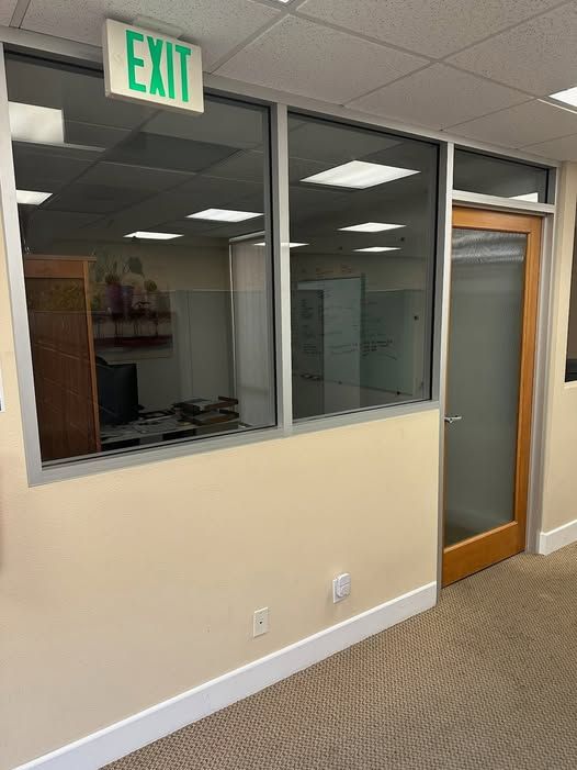 Office interior with an exit sign, glass windows, and a door. Beige walls and carpet.