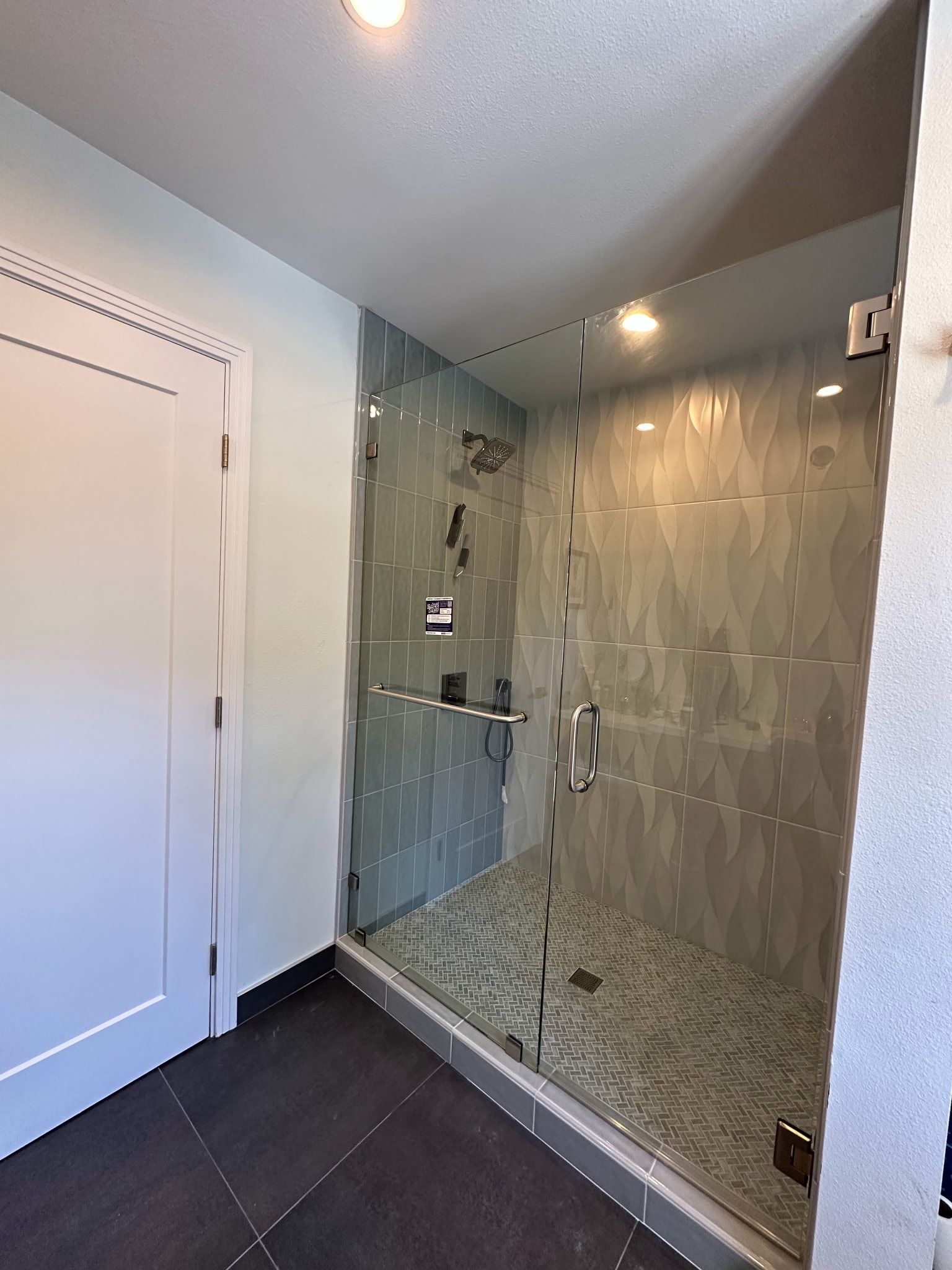 Modern bathroom with glass shower, gray tile, and dark floor.