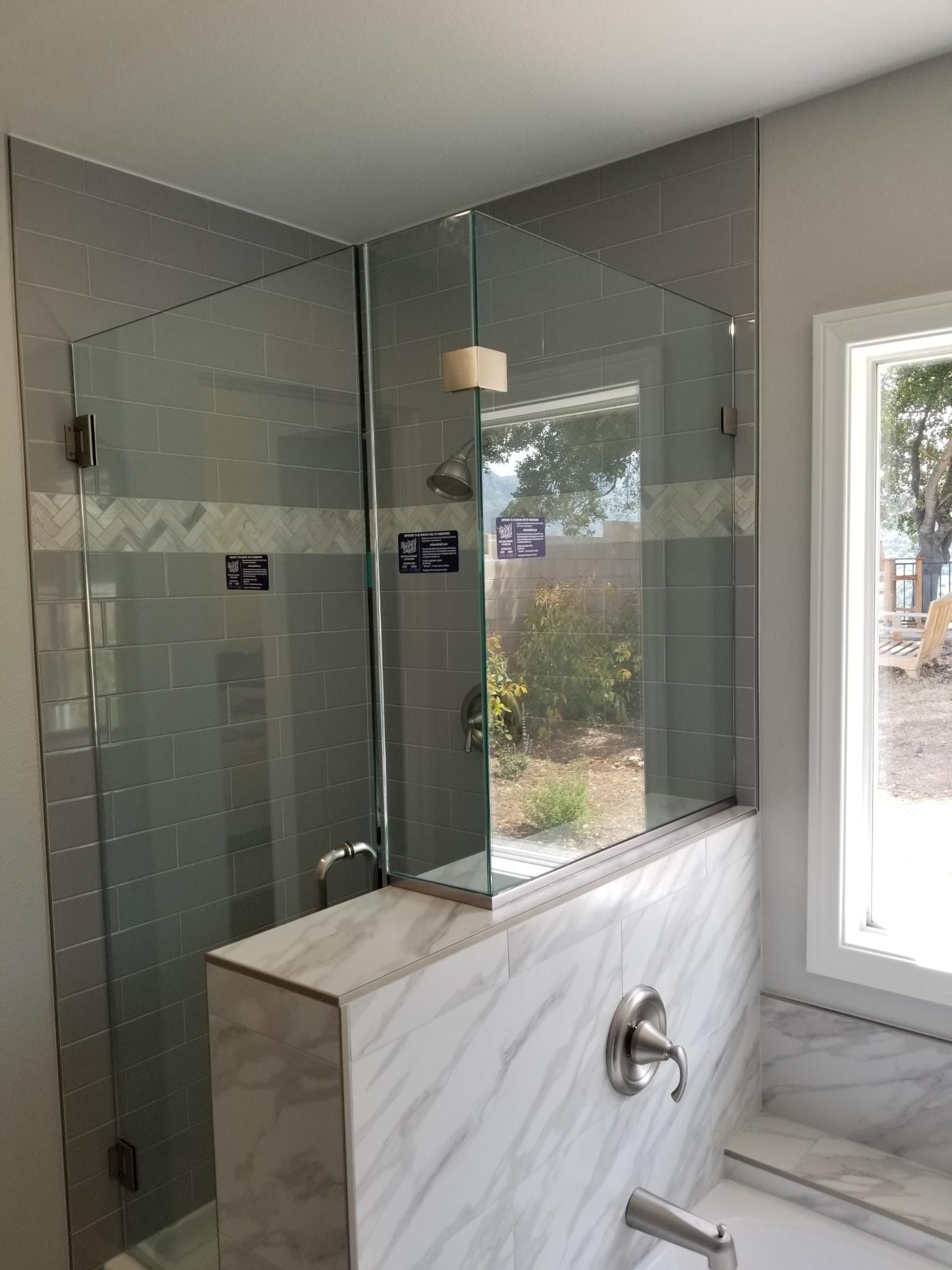 Corner glass shower enclosure with gray tiled walls and marble accents.