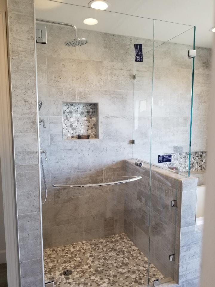 Modern shower with glass doors, gray tile walls, pebble floor, and built-in shelf.