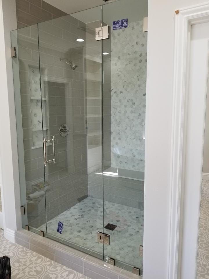 Glass shower enclosure with tiled walls and floor; inside a bathroom.