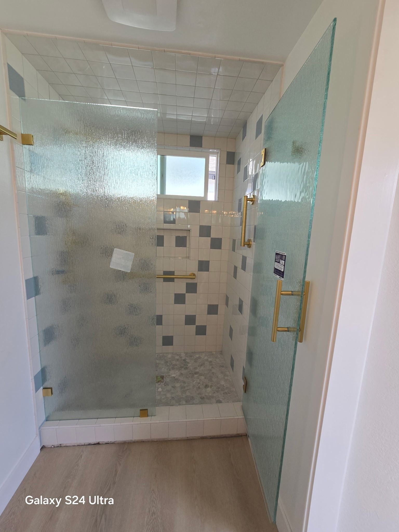 Shower with textured glass doors and white and blue tiled walls. Gold fixtures.