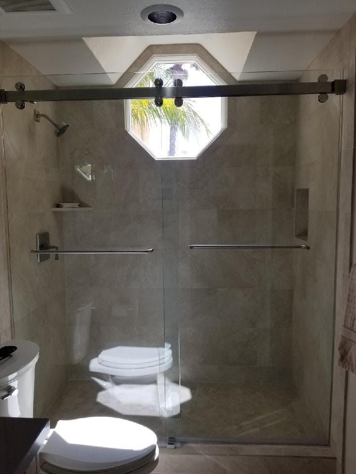 Bathroom with a clear glass shower, stone tiles, and an octagonal window above.