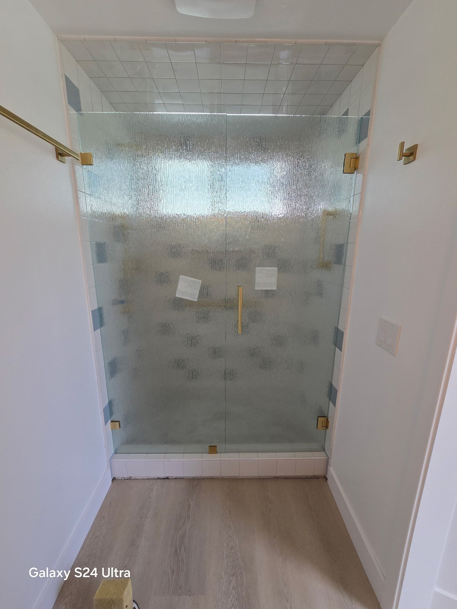 Shower stall with frosted glass and gold hardware, set between white walls.