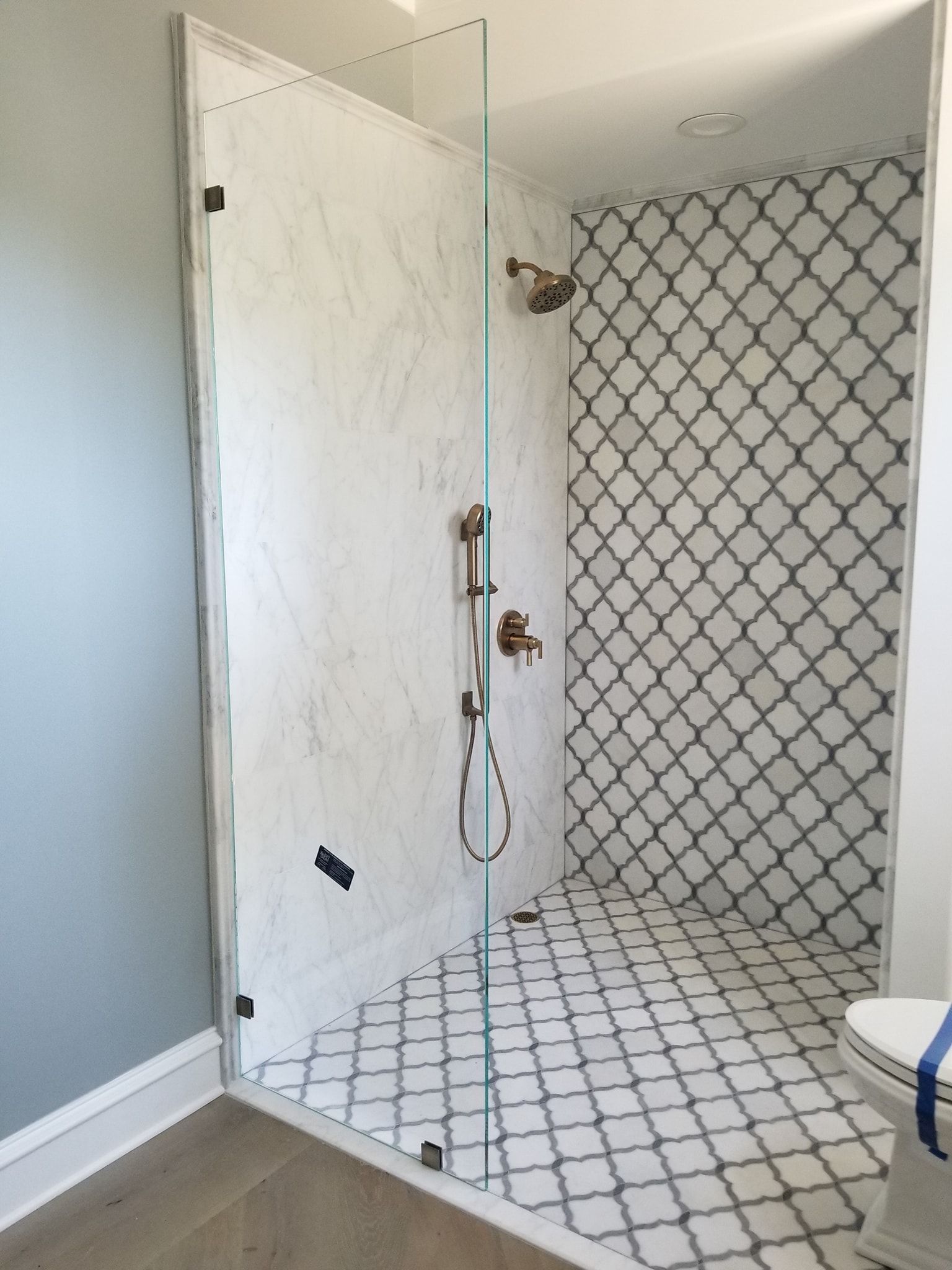 Modern bathroom with glass shower enclosure, marble and patterned tile.