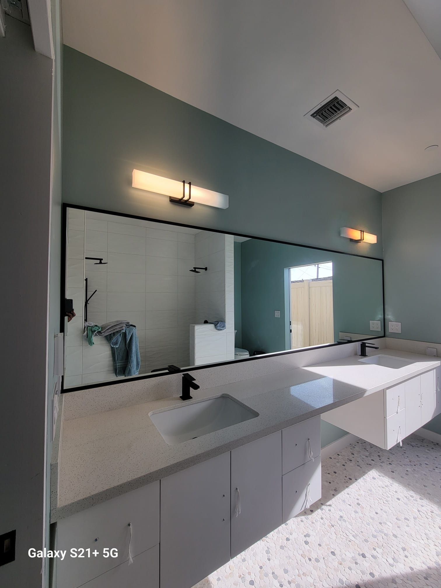 Bathroom with large mirror over white countertops, white cabinets, and mint-green walls.
