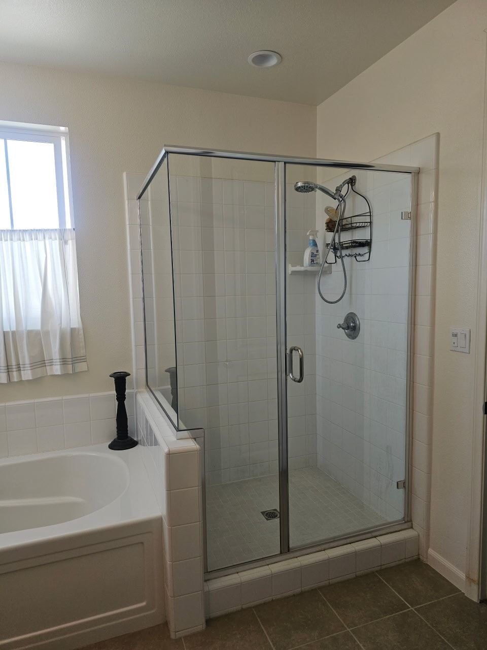 Bathroom with a glass-enclosed shower, a tub, and a window with a white curtain.