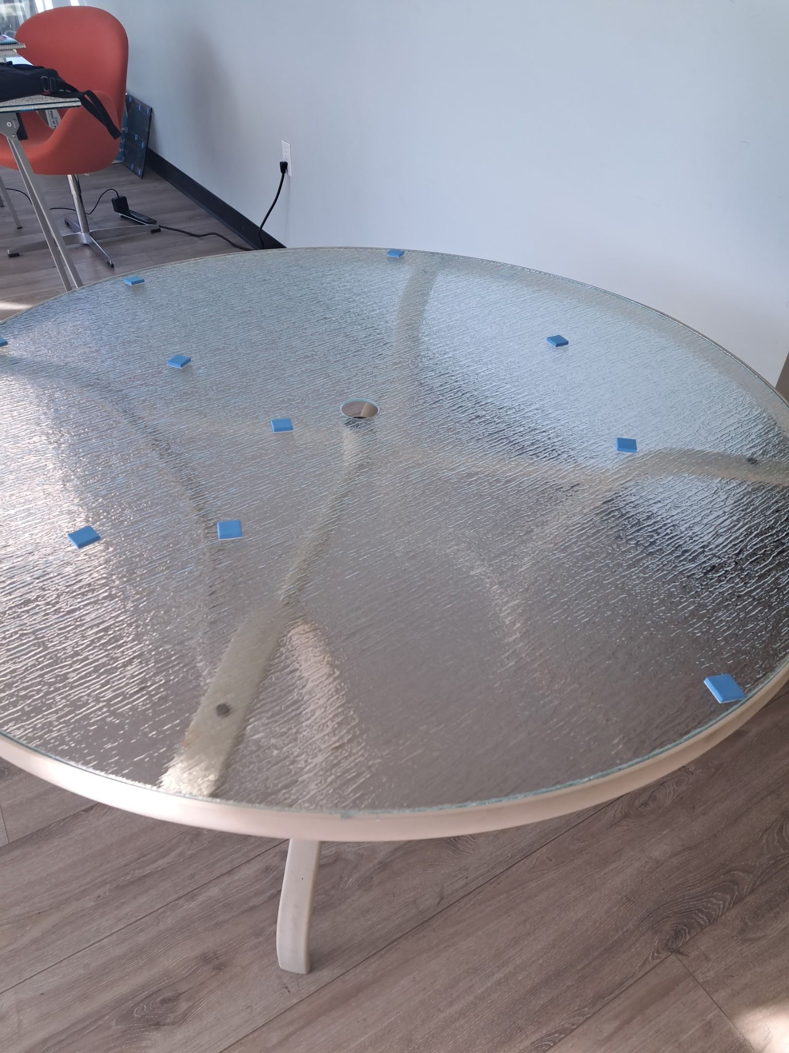 Round glass patio table with white legs, in a room with a chair.