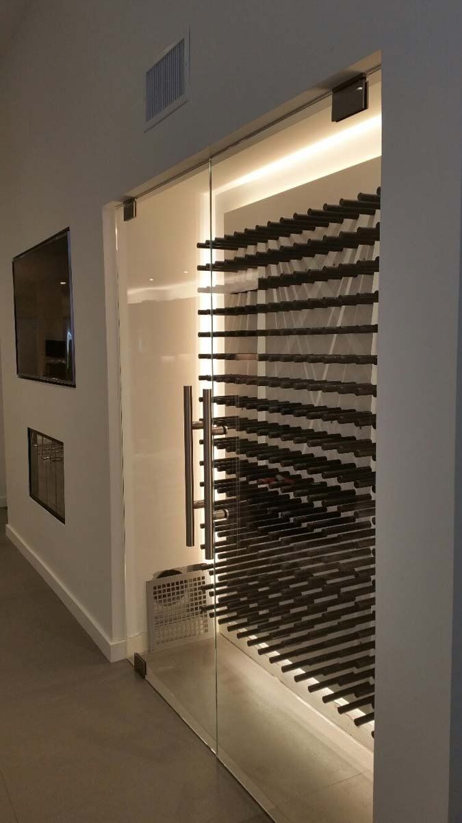 A modern wine cellar with glass door, rows of wine bottles, and warm lighting.