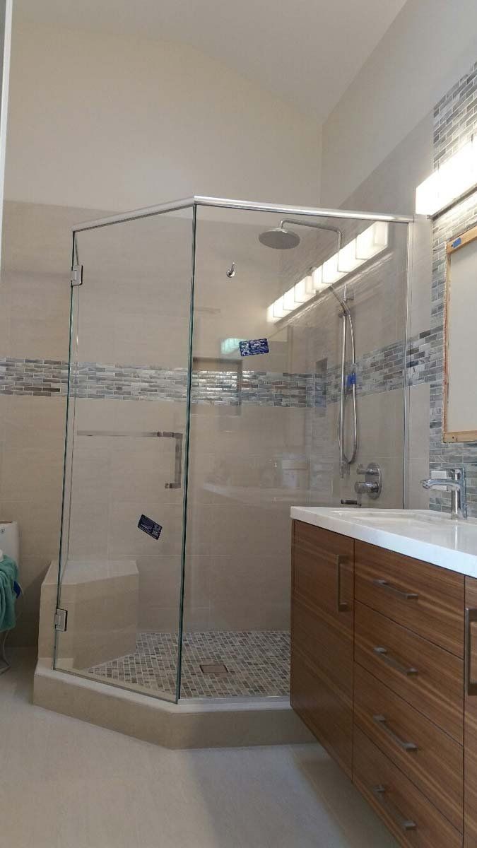 A glass corner shower with a stone floor in a bathroom. A wood vanity with a sink is beside it.