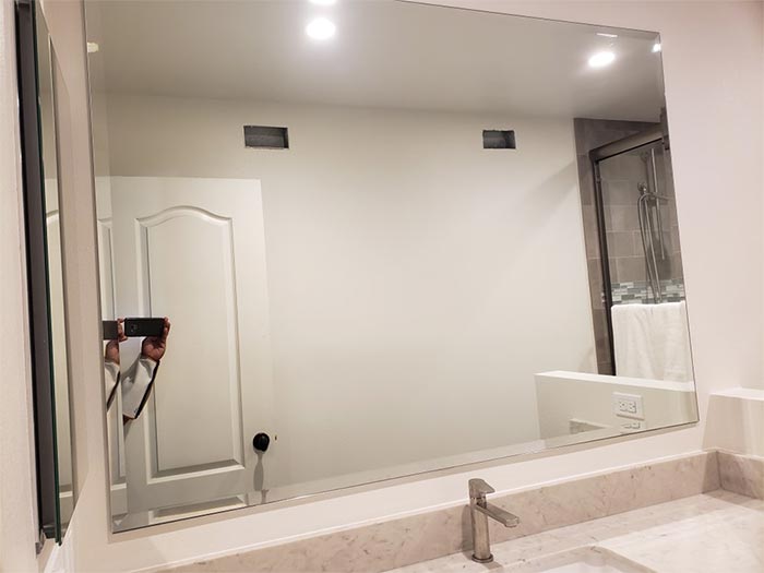 Bathroom with large mirror over sink; white walls, door, and counter.