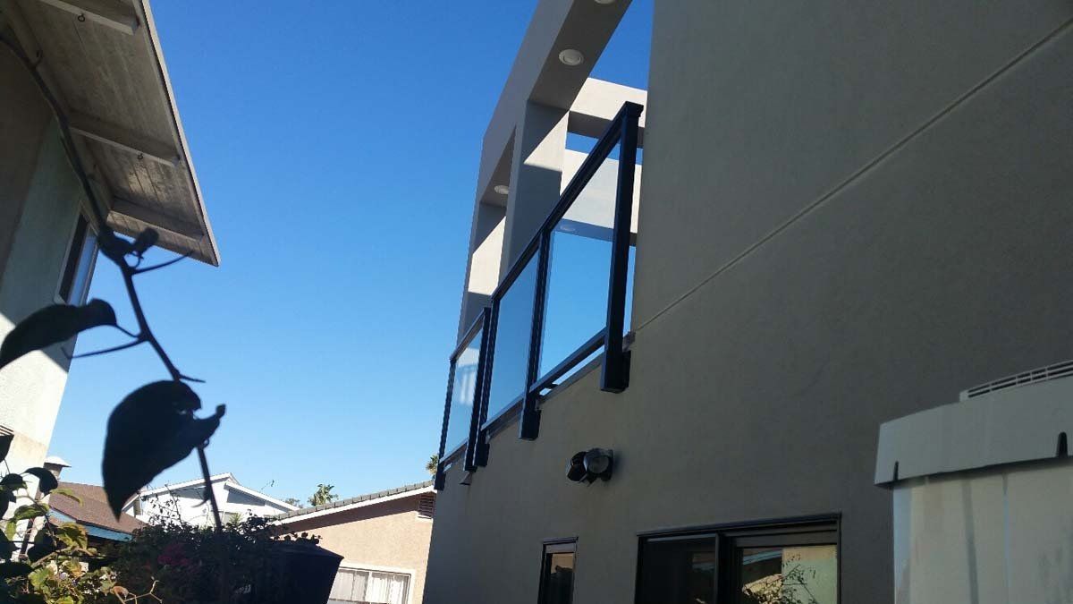 Exterior of a modern building with glass and black railing; clear blue sky.