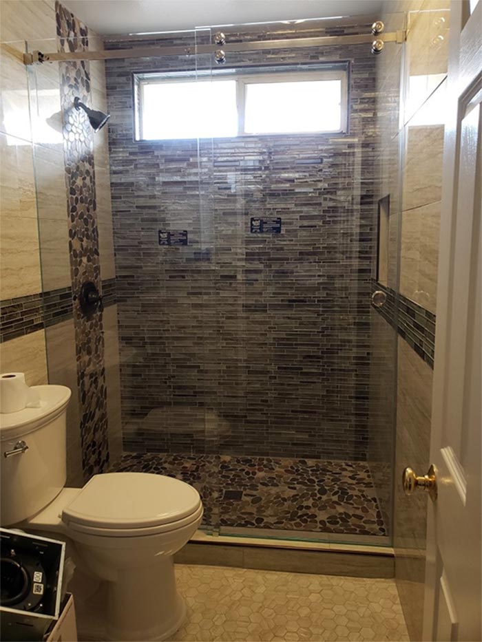 Bathroom with toilet and glass-enclosed shower featuring beige and brown tiling; small window above.