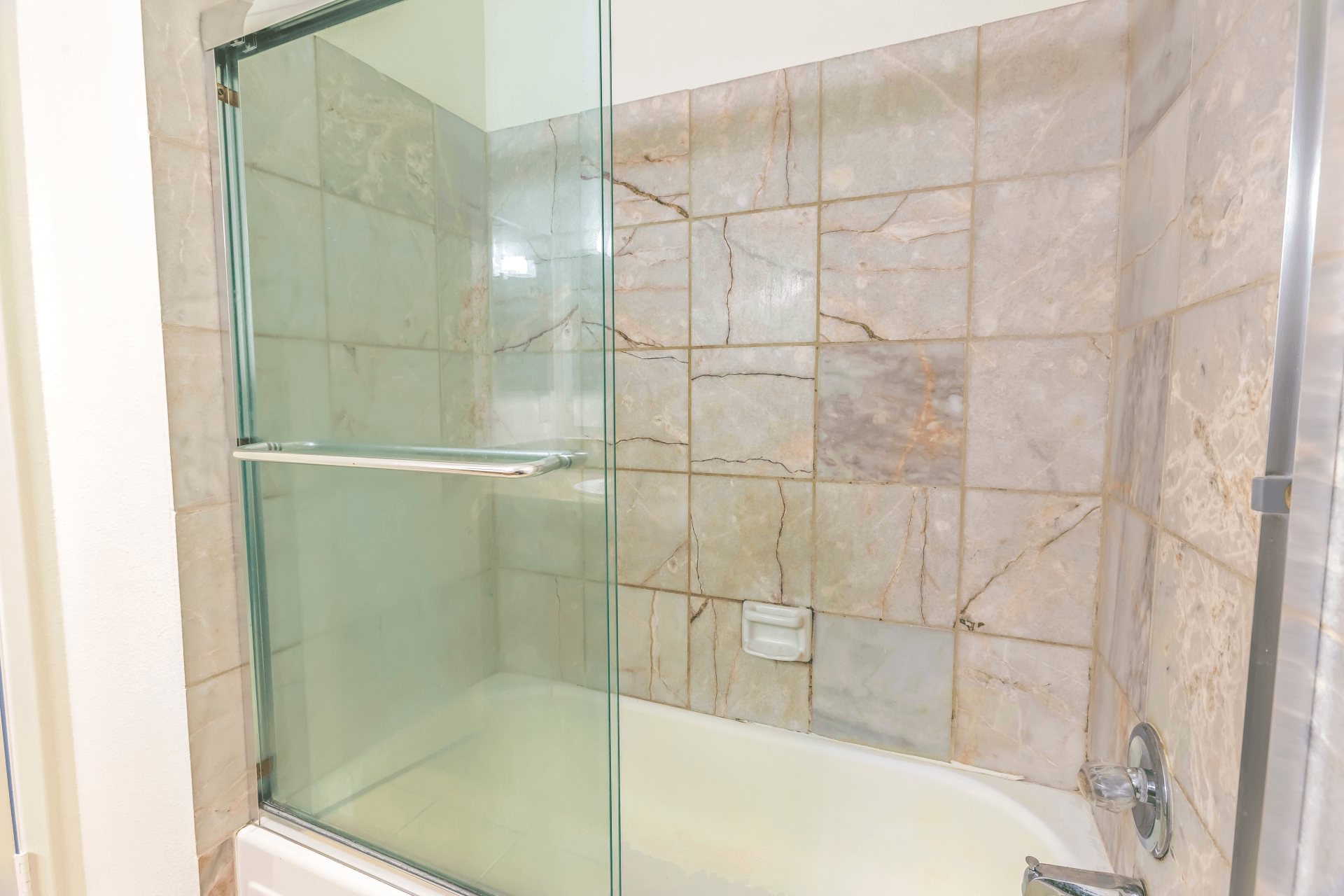 Shower stall with sliding glass doors, beige tile walls, and a white bathtub.