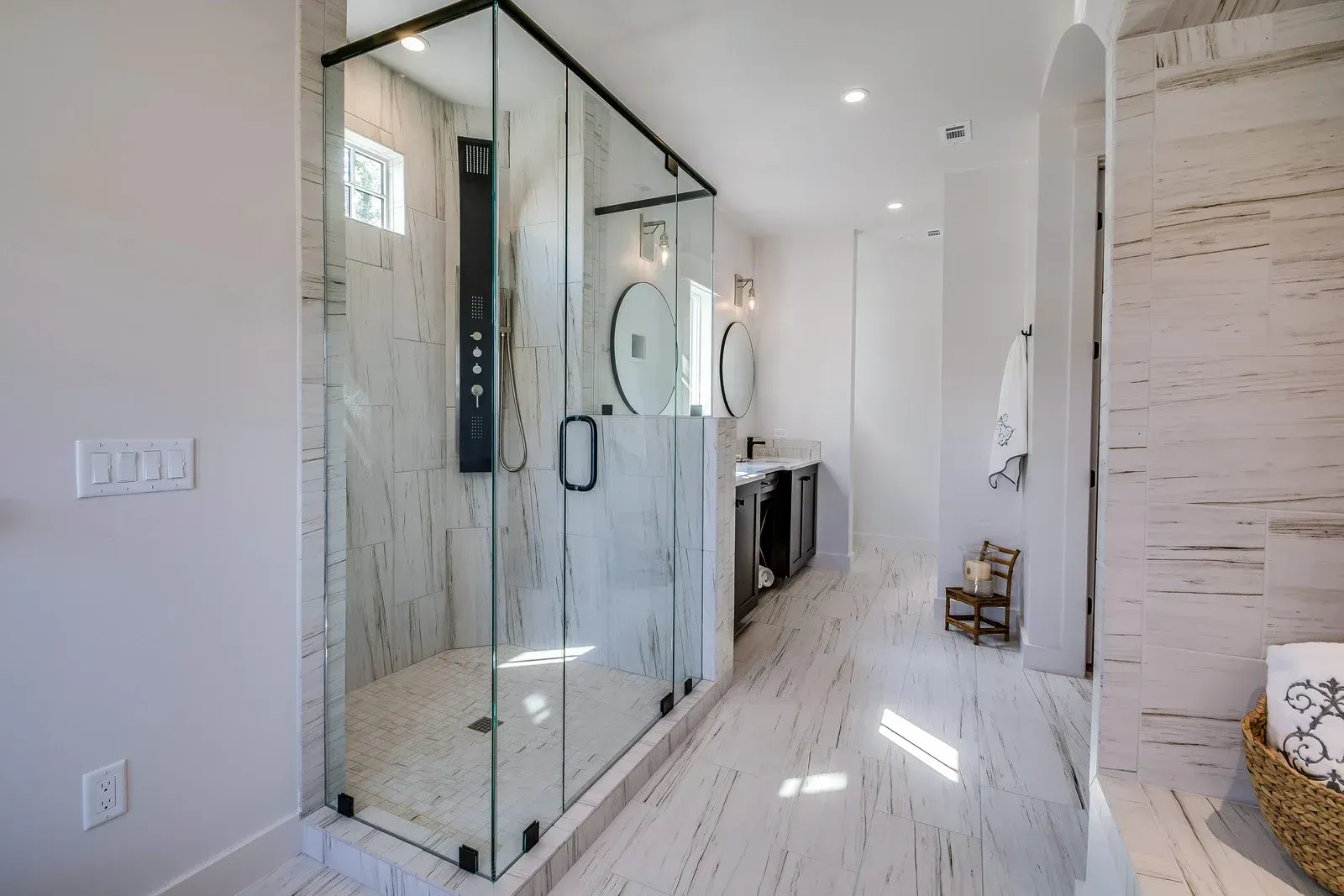 Spacious modern bathroom with large glass shower, marble walls, and double vanity.