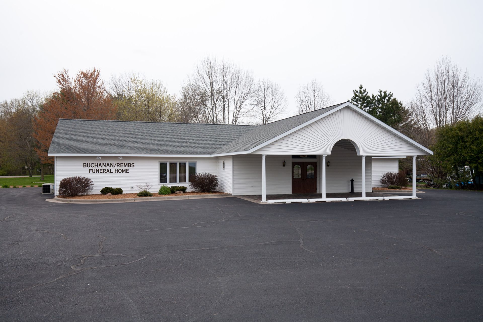 White Buchanan/Rembs Funeral Home building with gray roof and covered entrance.
