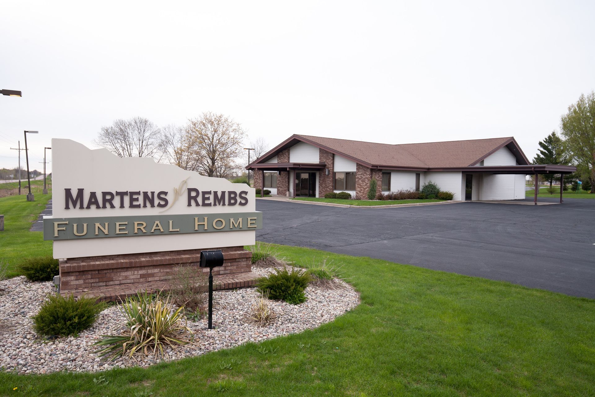 Sign for Martens Rembs Funeral Home in front of the building. Brown brick base, green lawn.